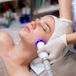 A young beautiful girl lies on the beautician's table and receives procedures with a professional apparatus for skin rejuvenation and moisturizing